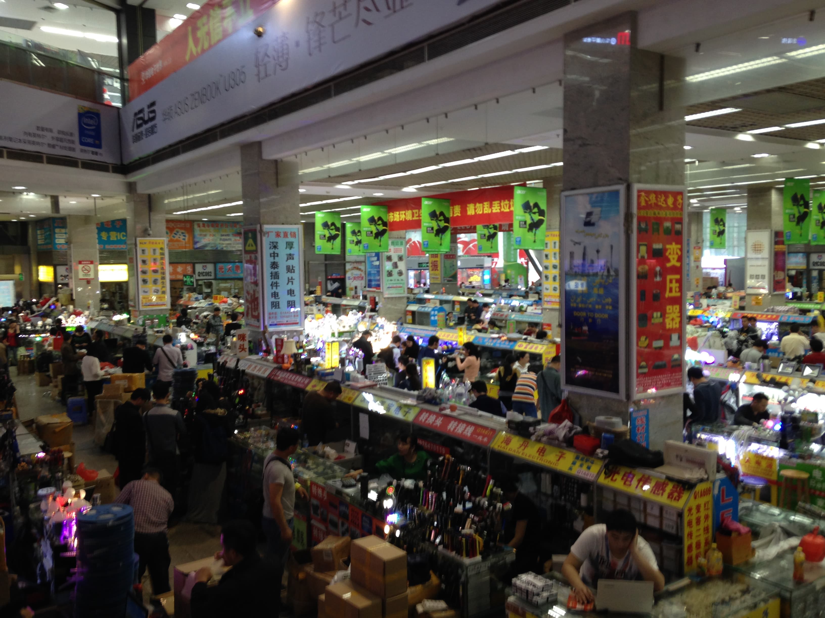 Wnętrze hali Huaqiang Electronic World w Shenzhen: rzędy stoisk z elektroniką, kartonami i chińskimi szyldami